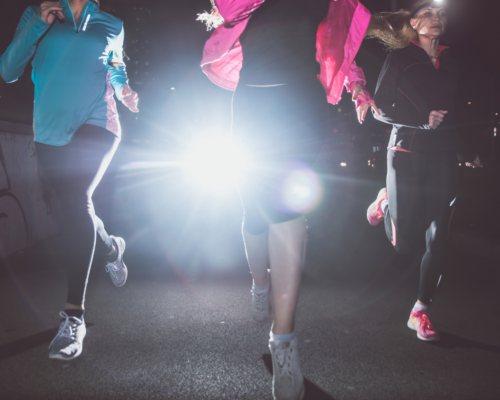 Three runners at night with a headlight in the background.